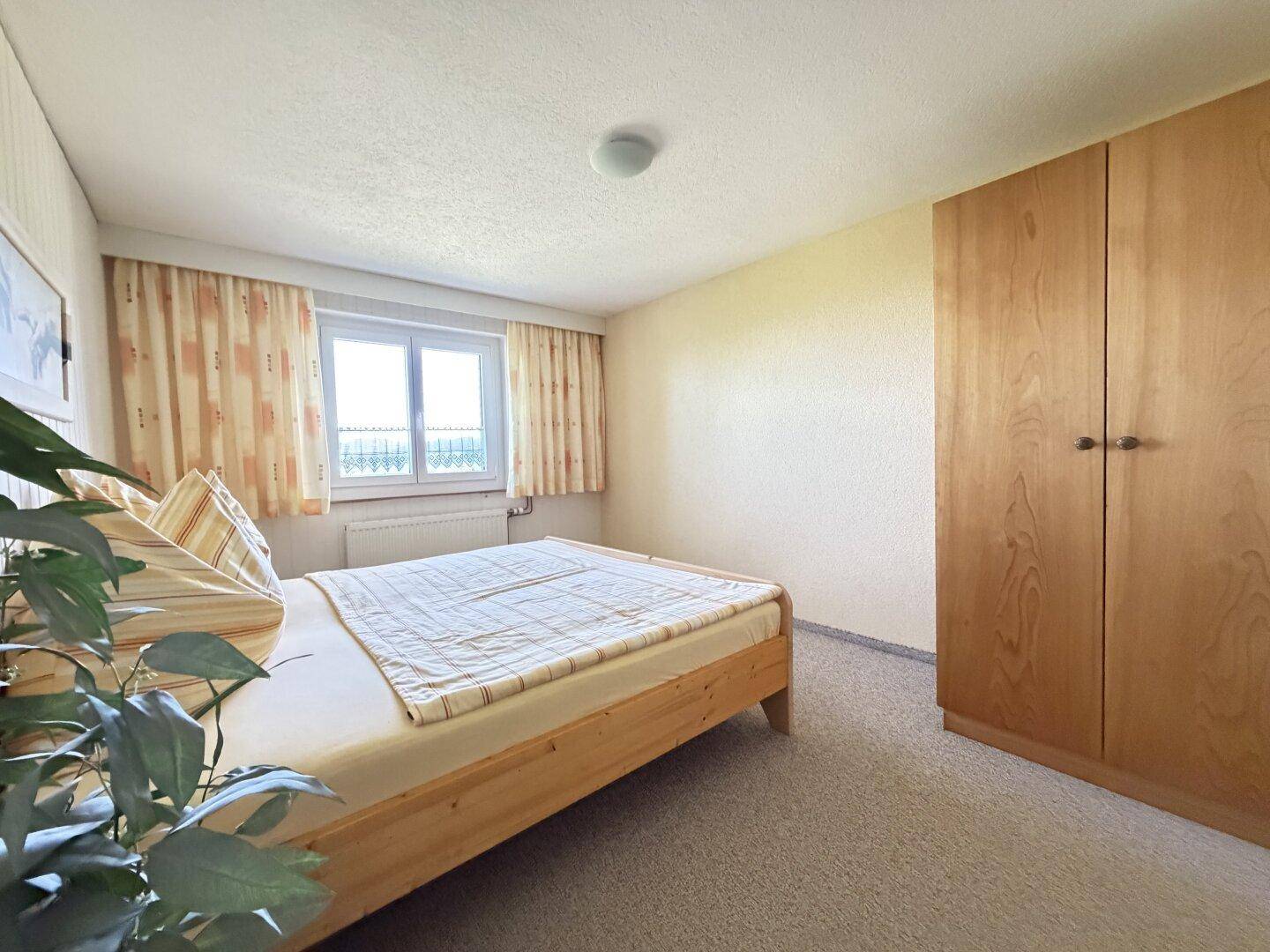 Helles Schlafzimmer mit Fenster, Teppichboden und geräumigem Kleiderschrank.