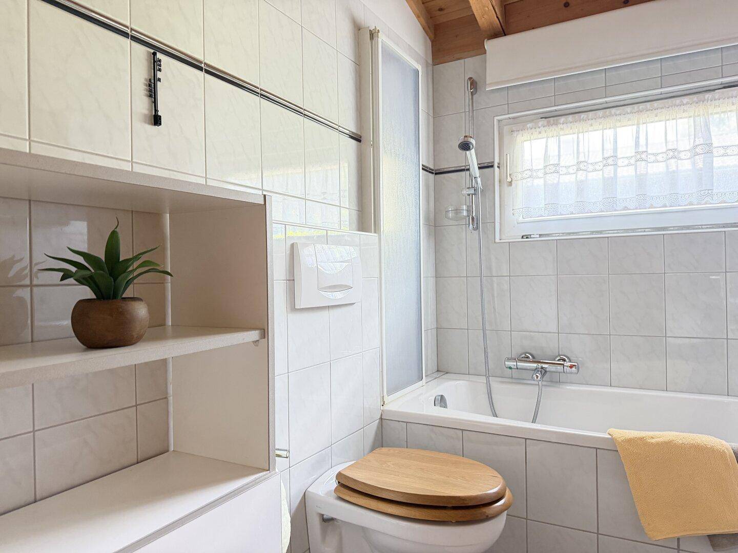 Helles Badezimmer mit Badewanne, WC und Fenster, klassisch gefliest.