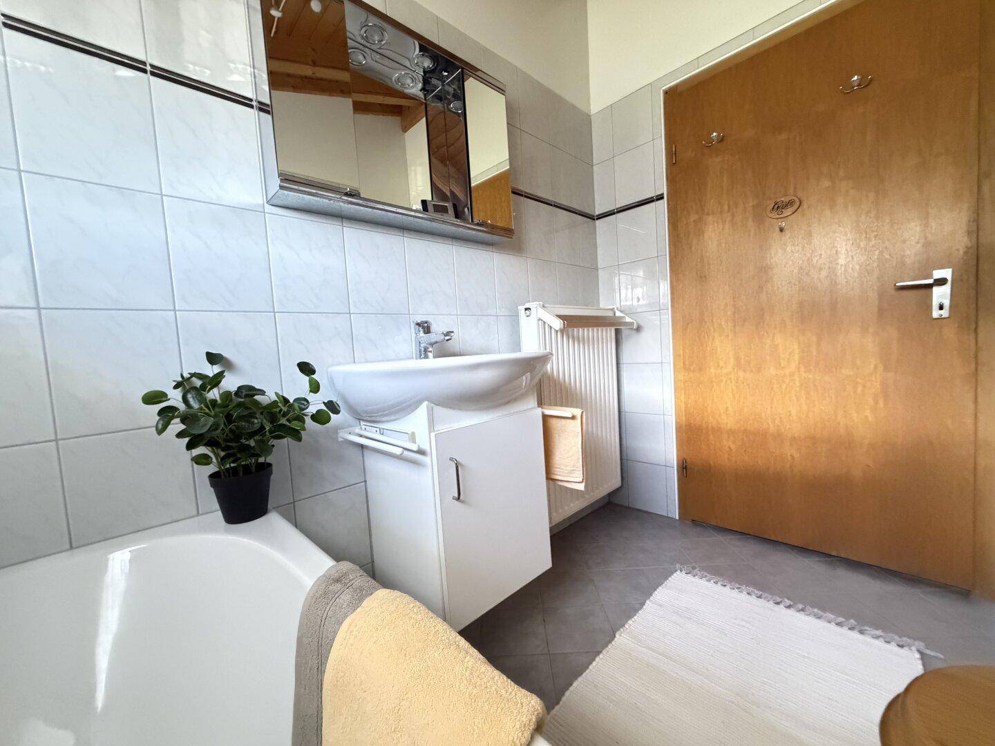 Funktionales Badezimmer mit Waschbecken, Spiegelschrank und Handtuchheizkörper.