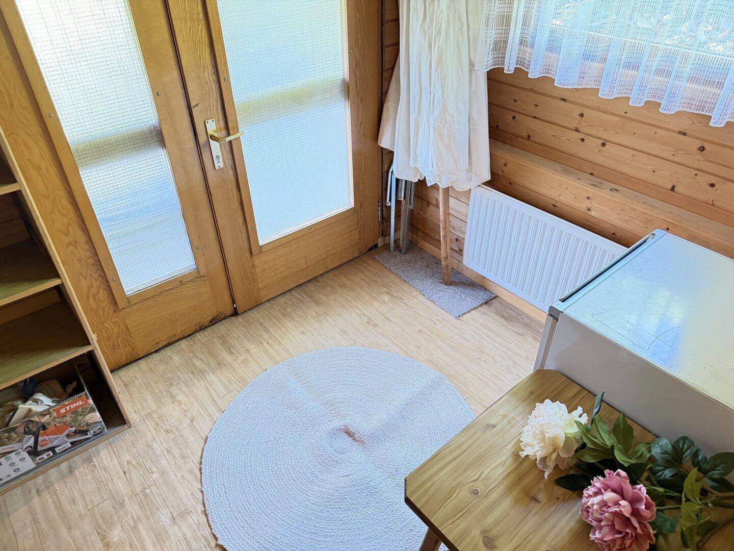 Kleiner Raum mit Holzverkleidung, Fenster und Tür, ideal als Abstellraum.