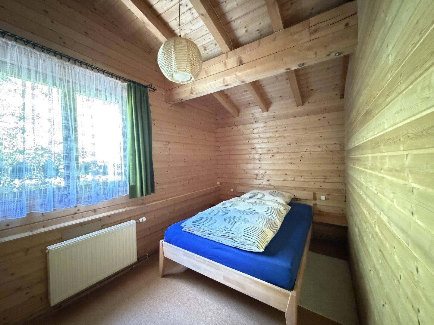 Gemütliches Schlafzimmer mit Holzvertäfelung, Einzelbett und Fenster.