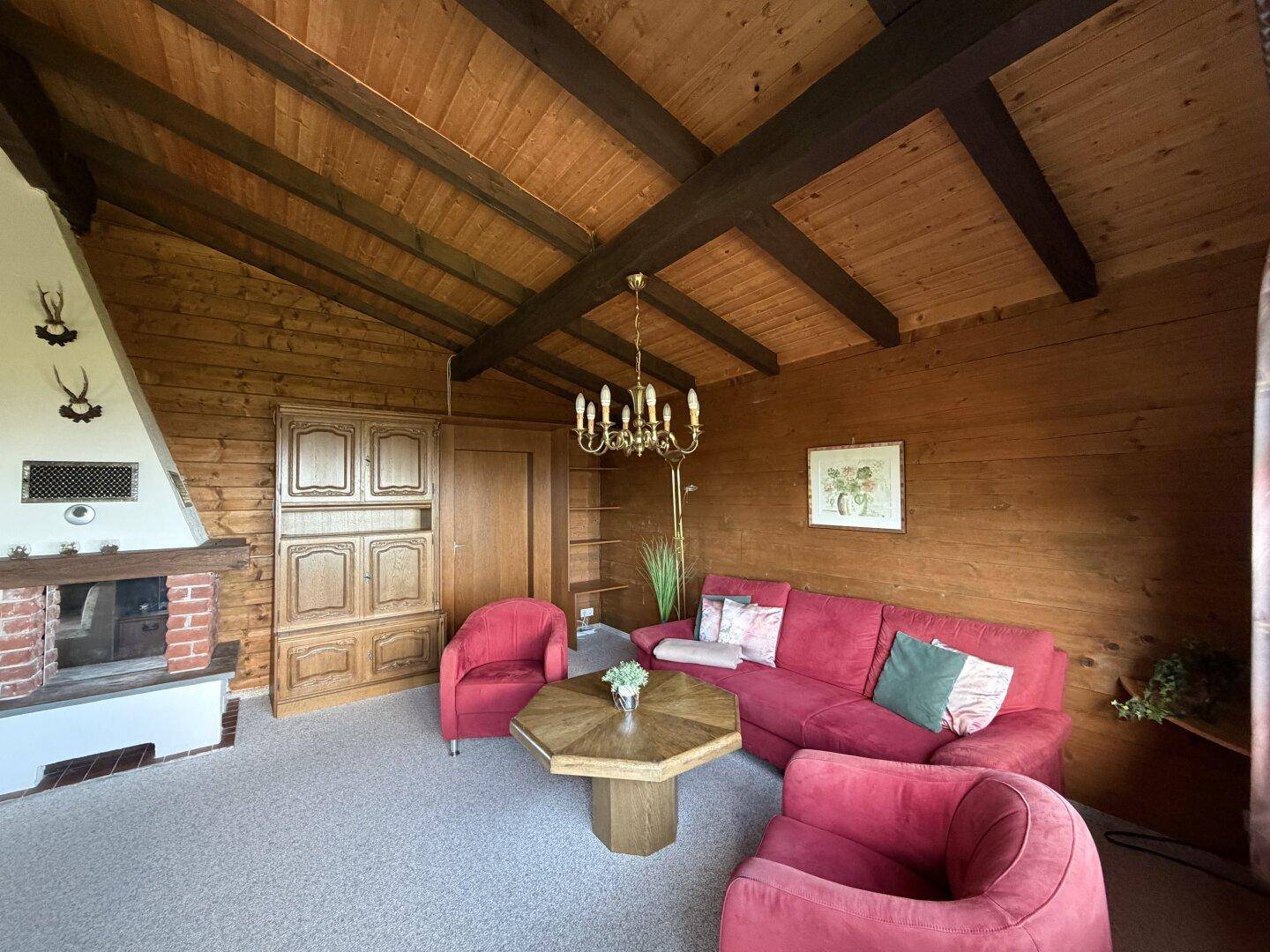 Einladendes Wohnzimmer mit roten Sofas, Holztisch und Kronleuchter, ergänzt durch einen Kamin.