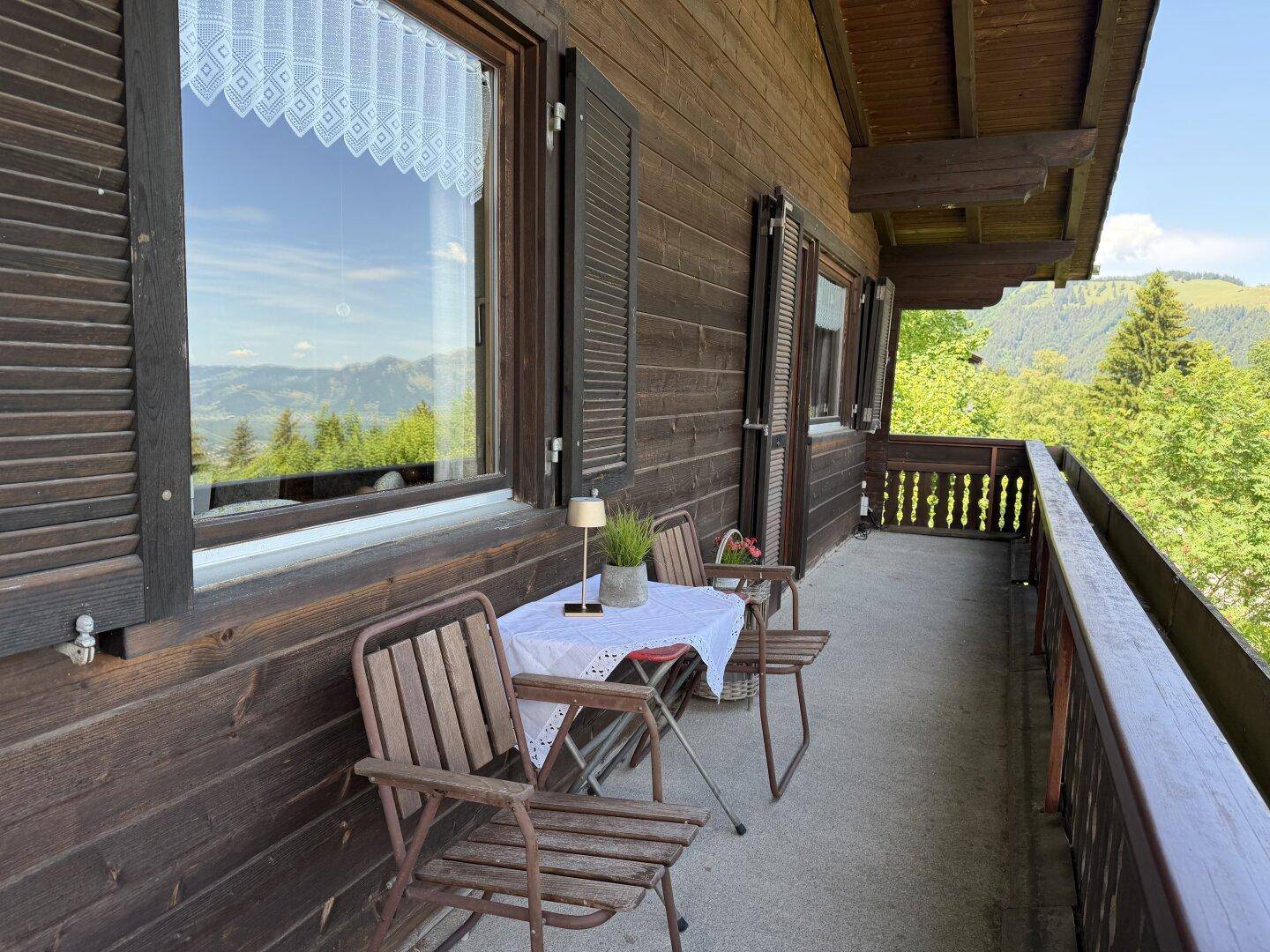 Balkon mit Sitzgelegenheiten, Holzfassade mit Fensterläden und weitem Bergblick.