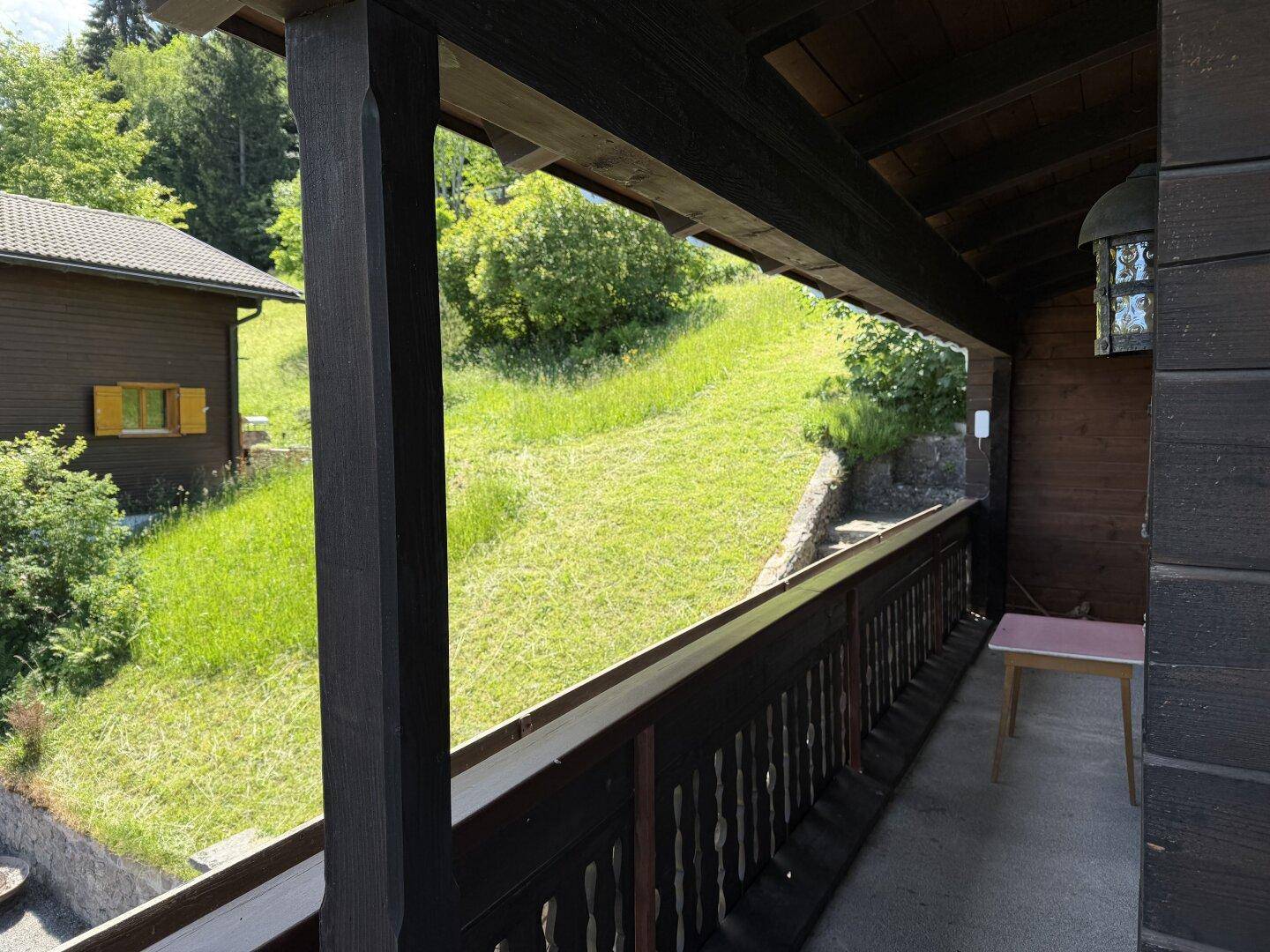 Balkon mit Blick auf einen grünen Hang, umgeben von Holzgeländer und tragenden Balken.