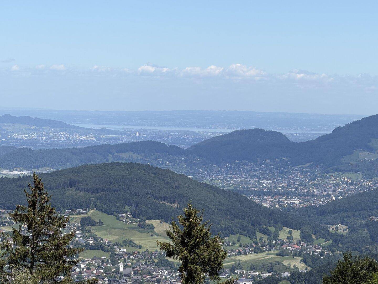 Panoramablick über ein Tal mit Stadt, Hügeln und einem entfernten See.