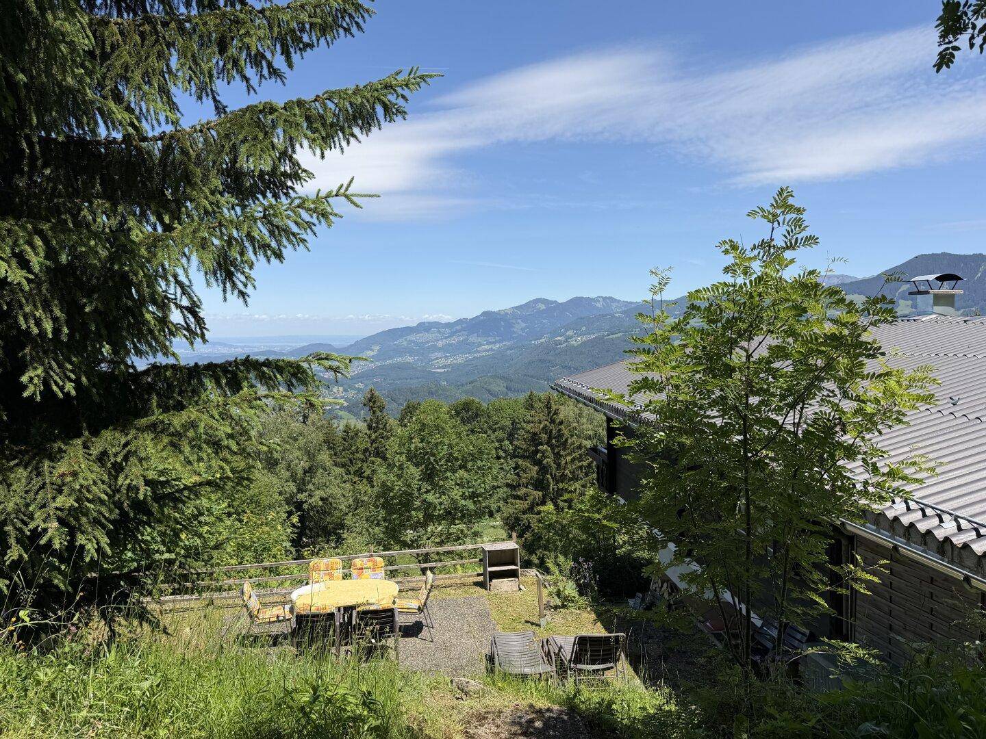 Große Terrasse mit Sitzgelegenheiten und weitem Blick über das Tal und den See.