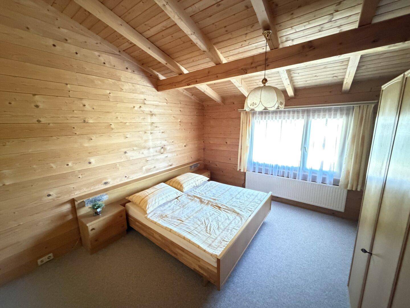 Rustikales Schlafzimmer mit Holzbalkendecke, Holzvertäfelung und Doppelbett.
