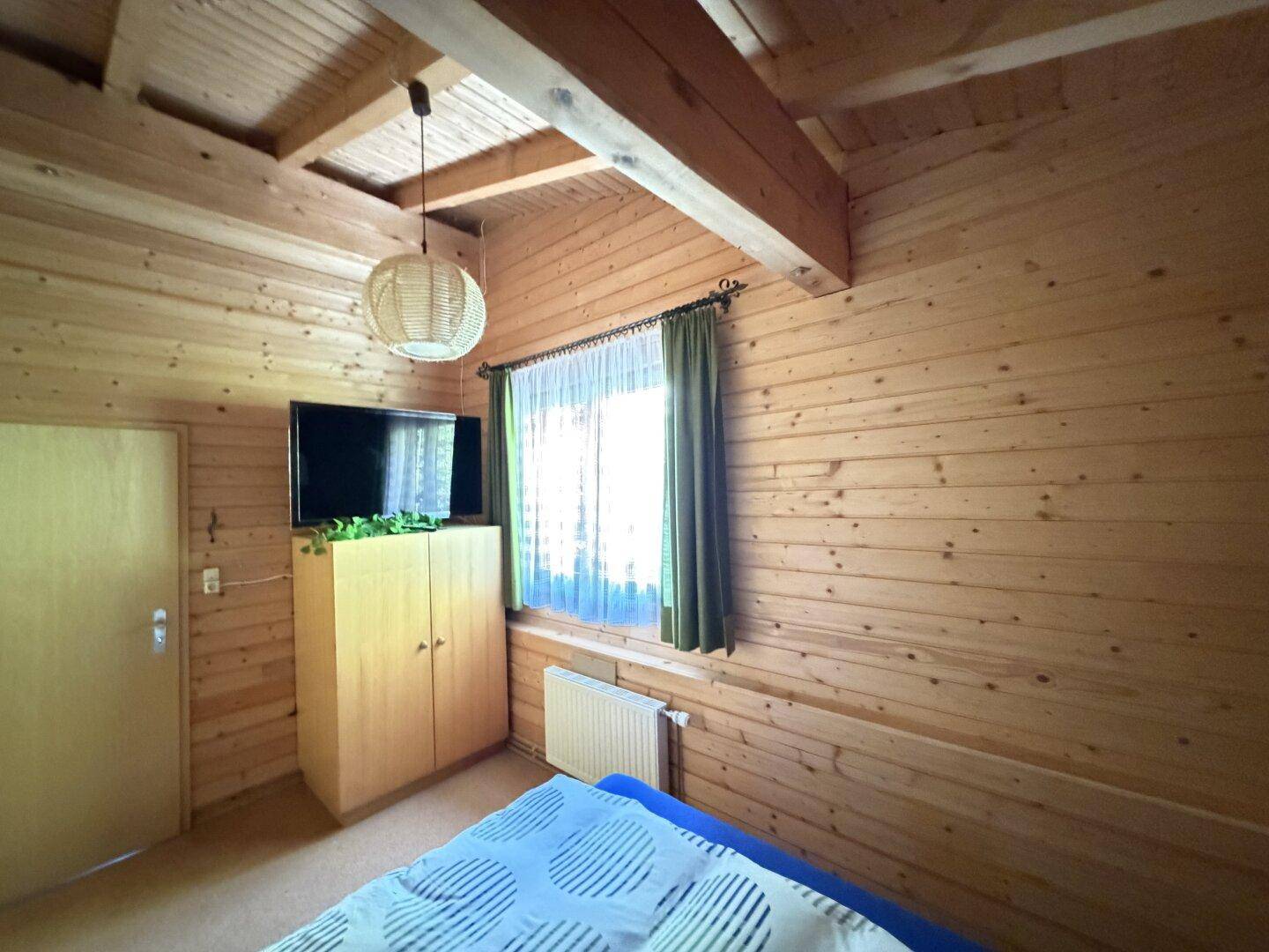 Schlafzimmer mit Holzwänden, Fernseher und Blick ins Grüne.