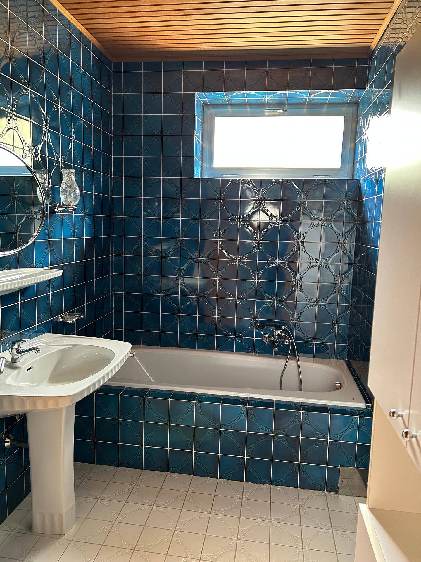 Badezimmer mit blauen Fliesen, Badewanne und Fenster für Tageslicht.