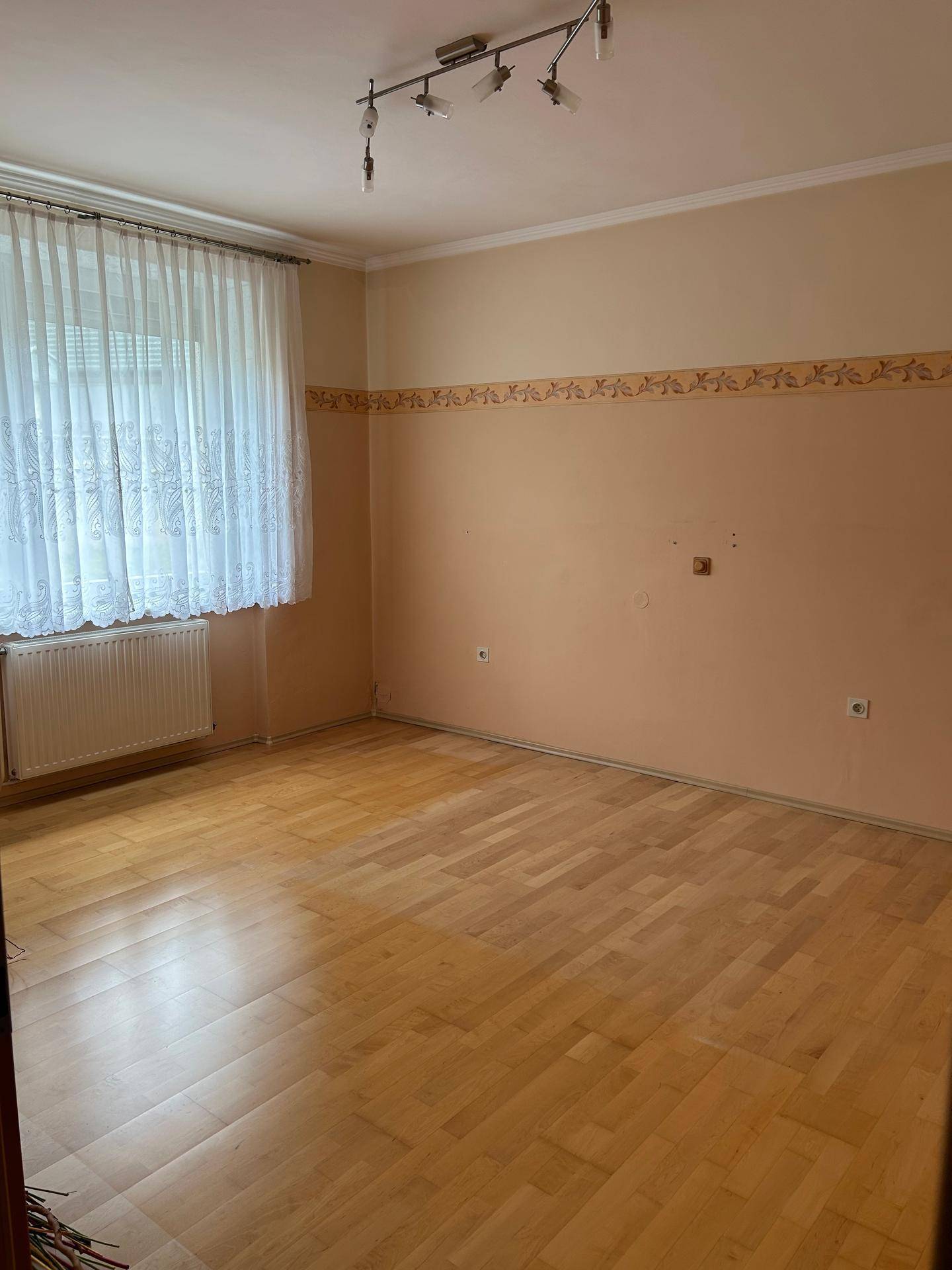 Leeres Zimmer mit hellem Parkettboden, neutralen Wänden und Fenster.