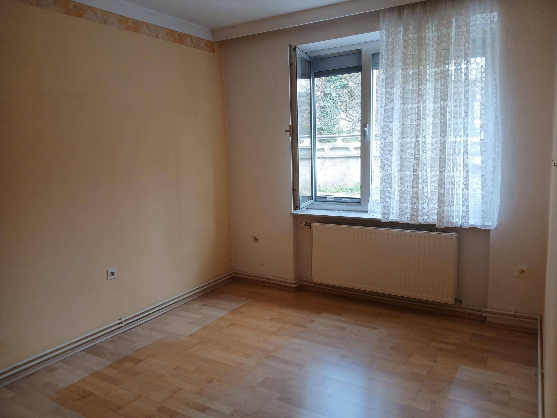 Helles Schlafzimmer mit Parkettboden und Fenster, bereit zur individuellen Gestaltung.