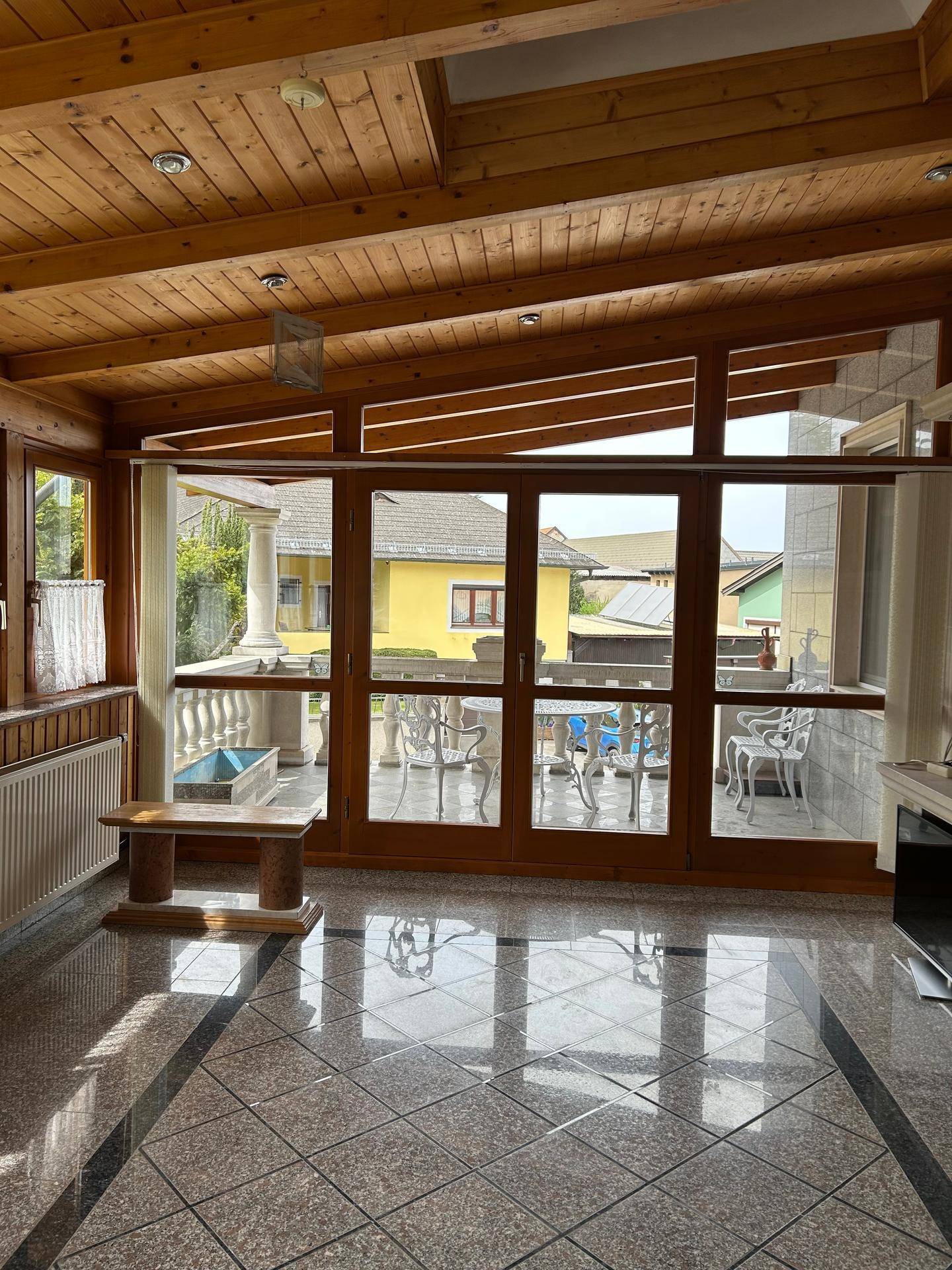 Heller Wintergarten mit Holzbalkendecke, Fliesenboden und Blick auf die Terrasse.