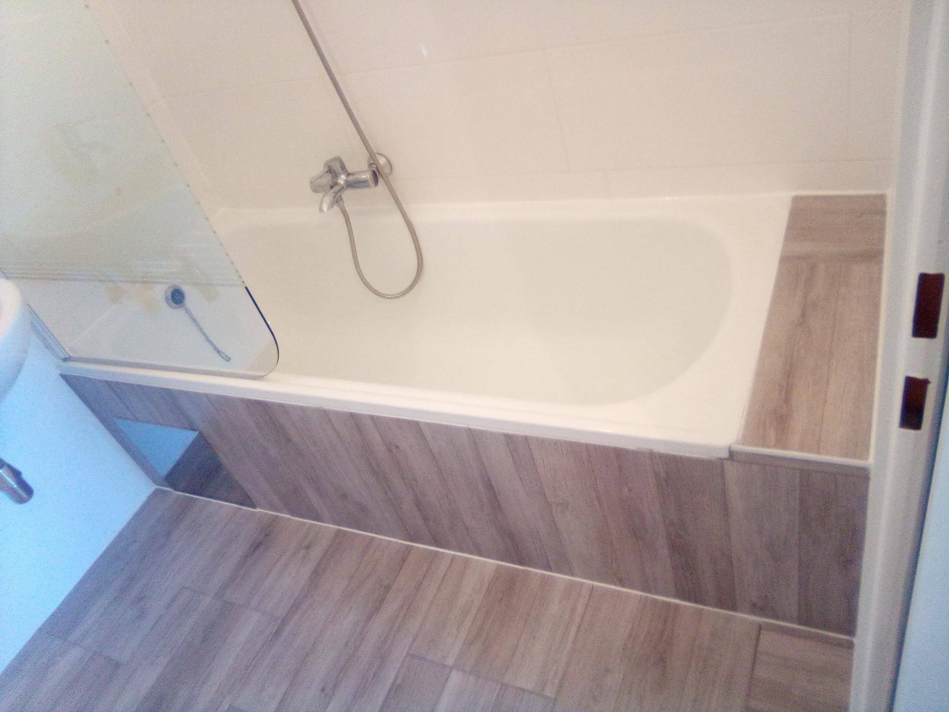 Modernes Badezimmer mit Badewanne und Duschfunktion, ausgestattet mit Holzoptik-Verkleidung und Fliesenboden.