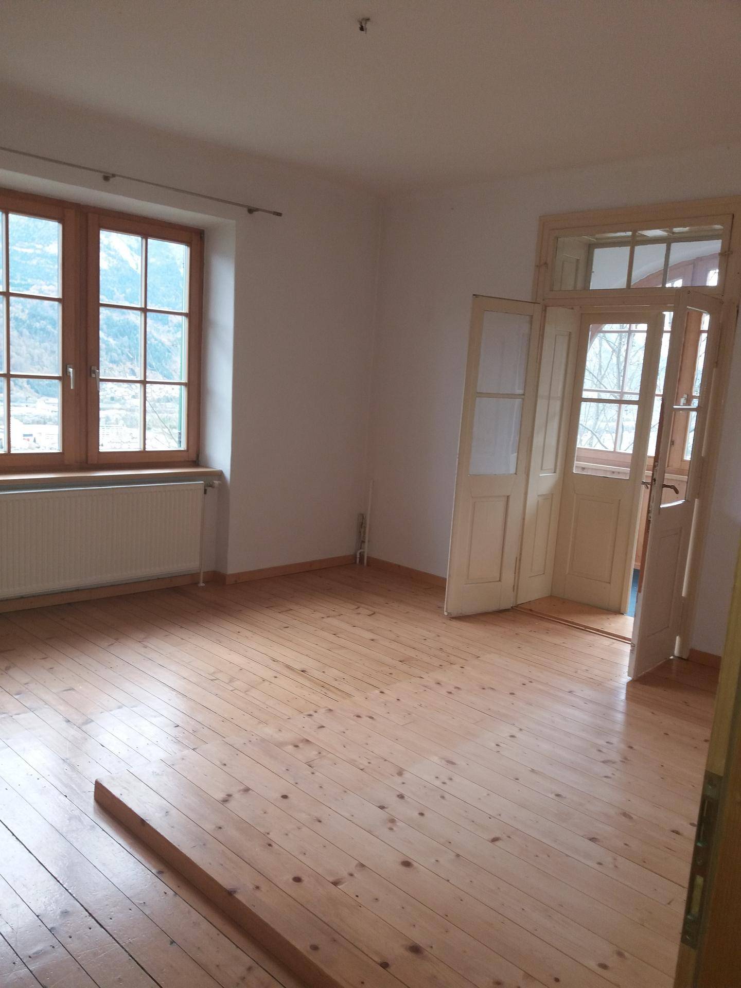 Geräumiger Raum mit Holzdielenboden und Doppeltüren, die zu einem weiteren Bereich führen.