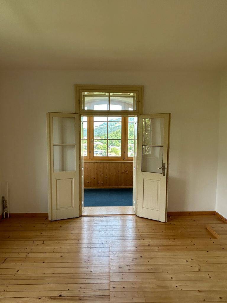 Geräumiger Raum mit Holzdielenboden und Doppeltüren, die zu einem hellen Erkerbereich führen.