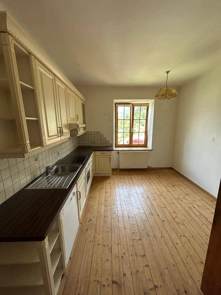 Helle Küche mit traditionellen Schränken, Holzdielenboden und einem Fenster mit Blick ins Grüne.