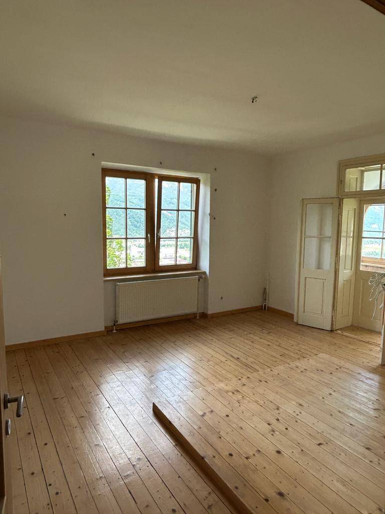 Heller Raum mit Holzdielenboden, Fenster und Heizkörper, mit Doppeltüren zu einem angrenzenden Bereich.
