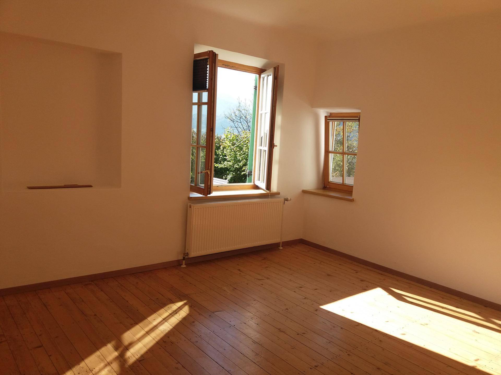 Sonniger Raum mit Holzdielenboden und geöffnetem Fenster, das viel natürliches Licht hereinlässt.