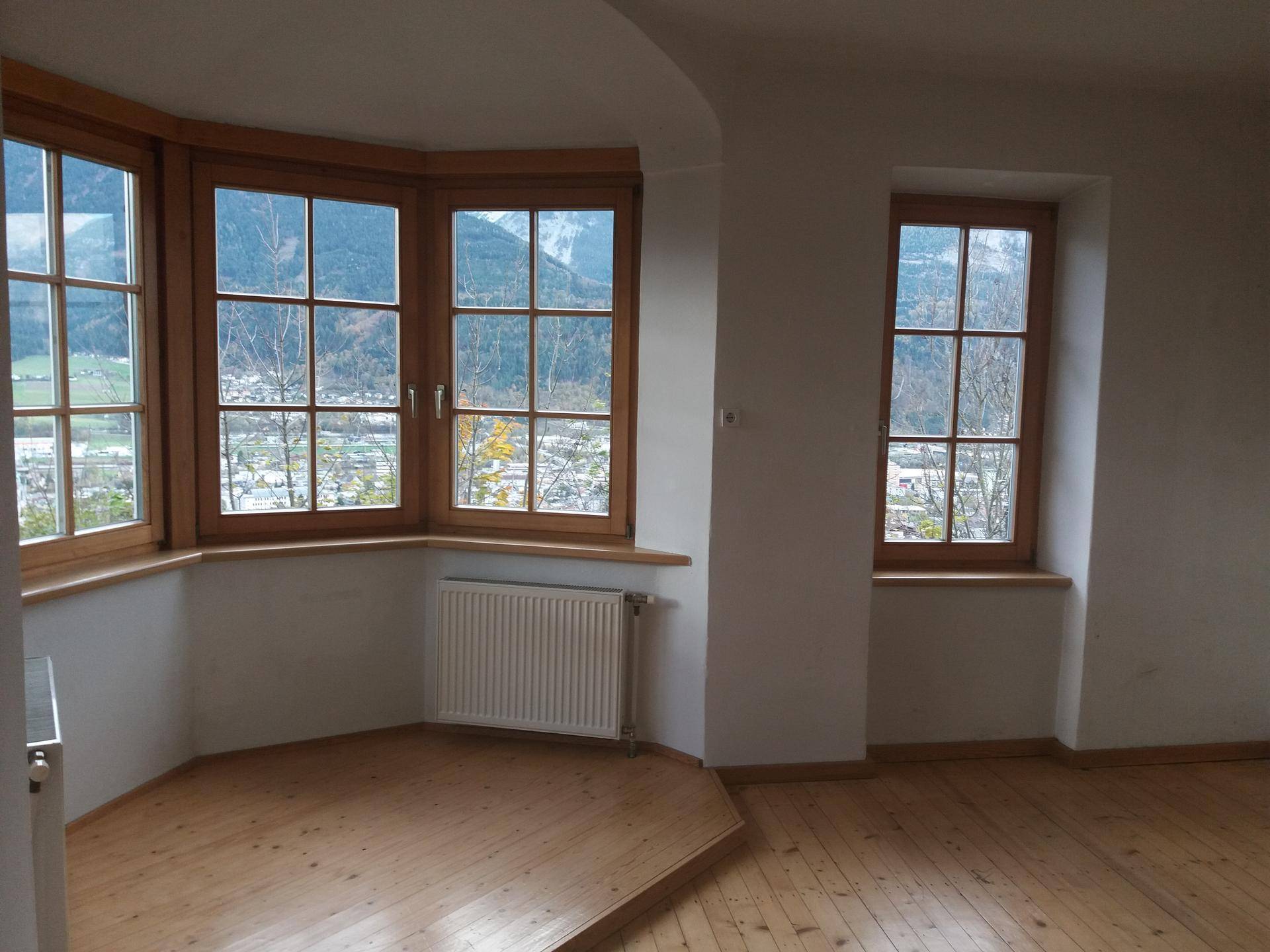 Heller Raum mit Holzdielenboden und Erkerfenstern, die einen malerischen Blick auf die Berge bieten.