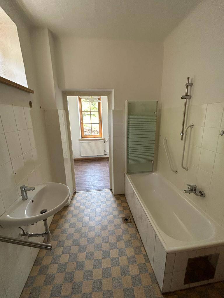 Badezimmer mit Badewanne, Waschbecken und karierten Fliesen, ausgestattet mit einem Handtuchheizkörper.