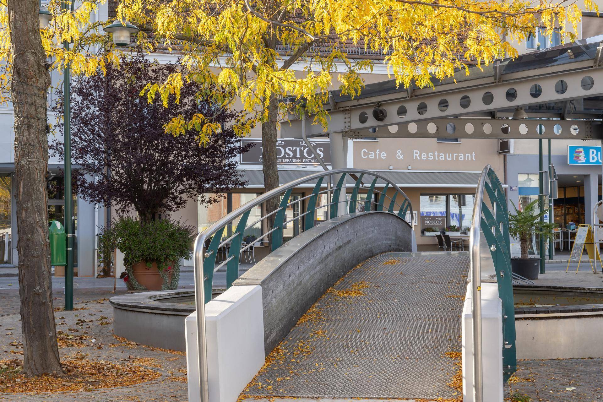 Eine städtische Szene mit einer kleinen Fußgängerbrücke und einem Café im Hintergrund.