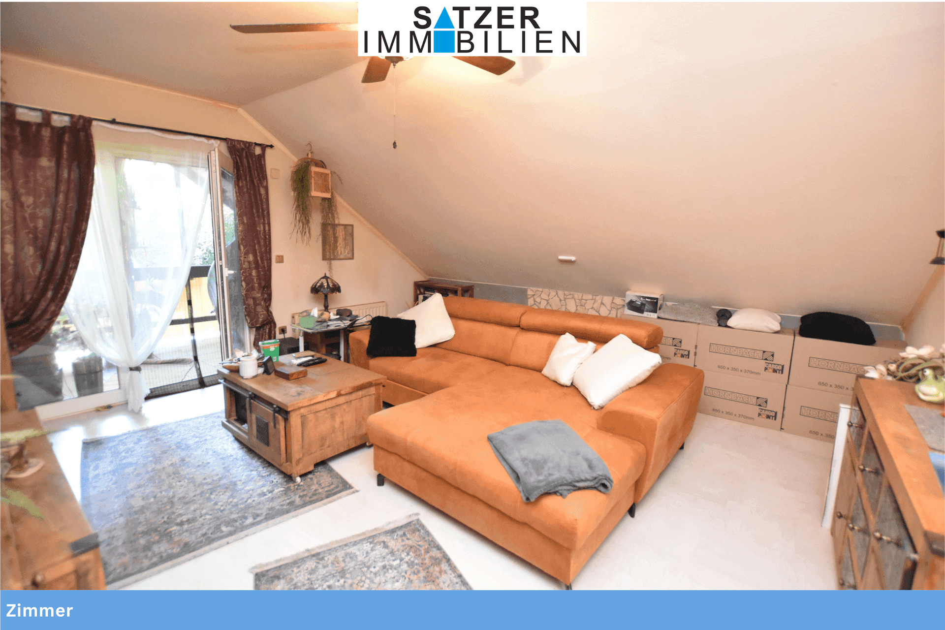Gemütlicher Wohnbereich im Dachgeschoss mit schräger Decke, großem Sofa und Zugang zur Terrasse.