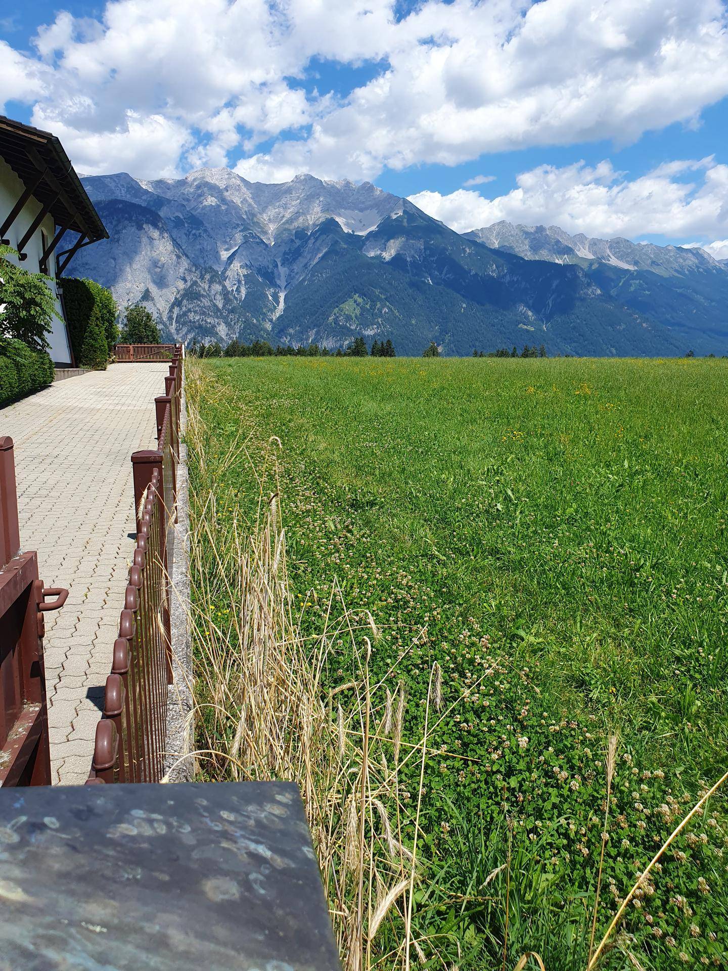 Gepflasterter Weg neben einem grünen Feld mit Blick auf die majestätischen Berge unter blauem Himmel.