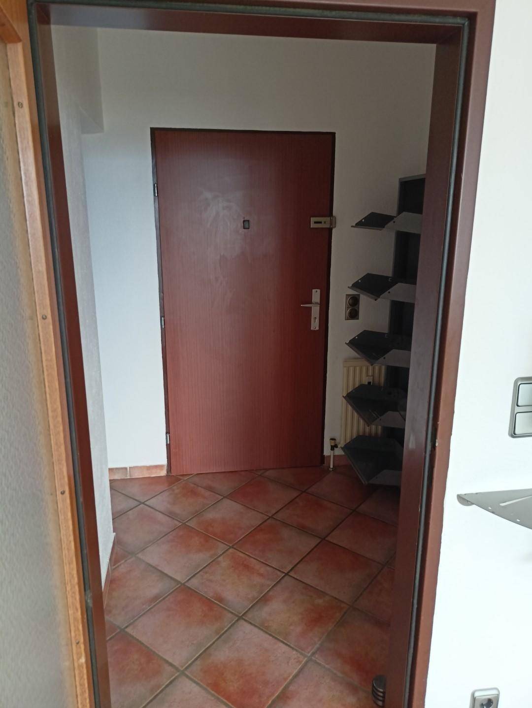 Eingangsbereich mit Terrakotta-Fliesenboden und einer robusten Holztür.