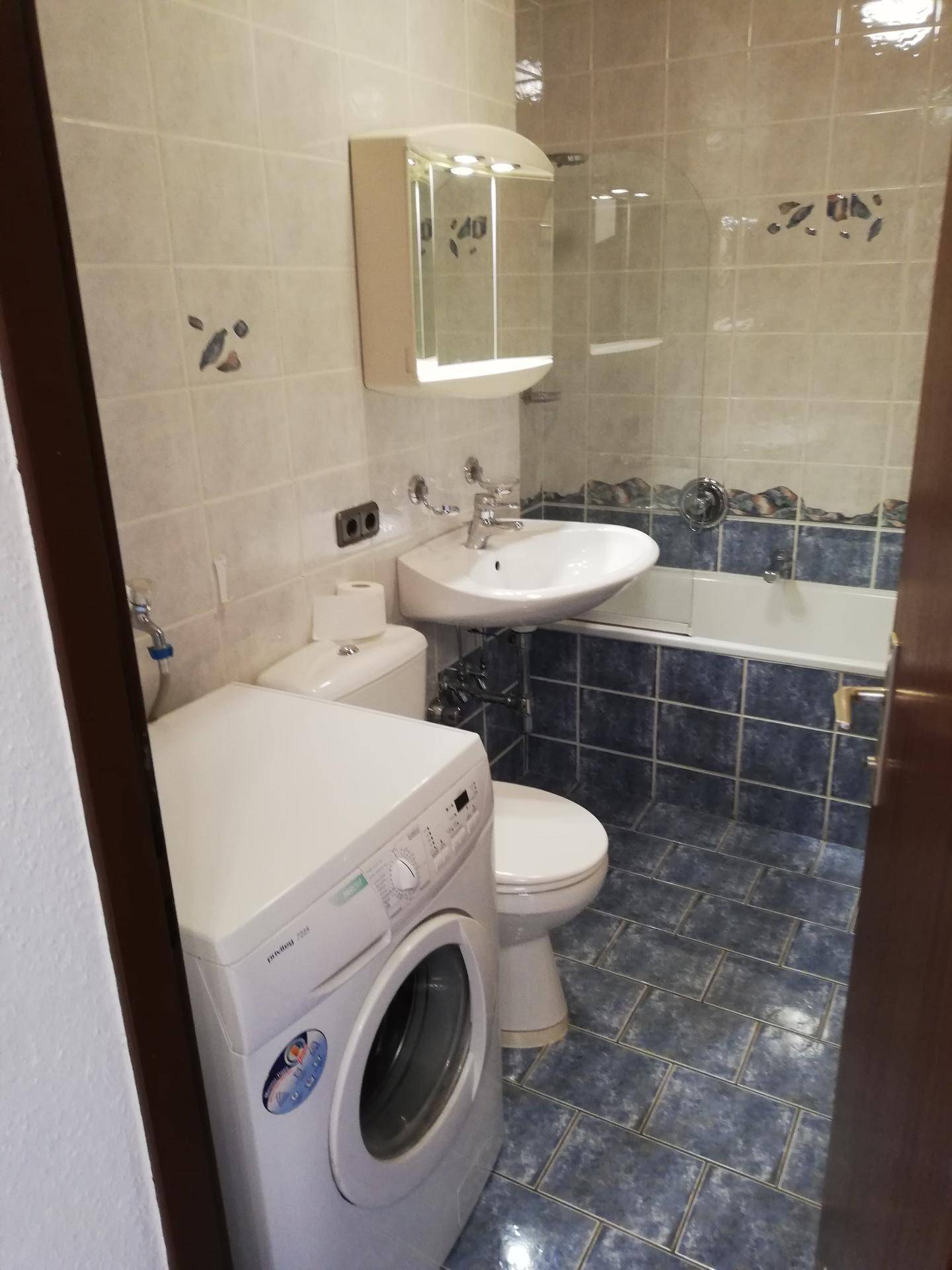 Badezimmer mit blauen und weißen Fliesen, Badewanne, WC, Waschbecken und Waschmaschine.