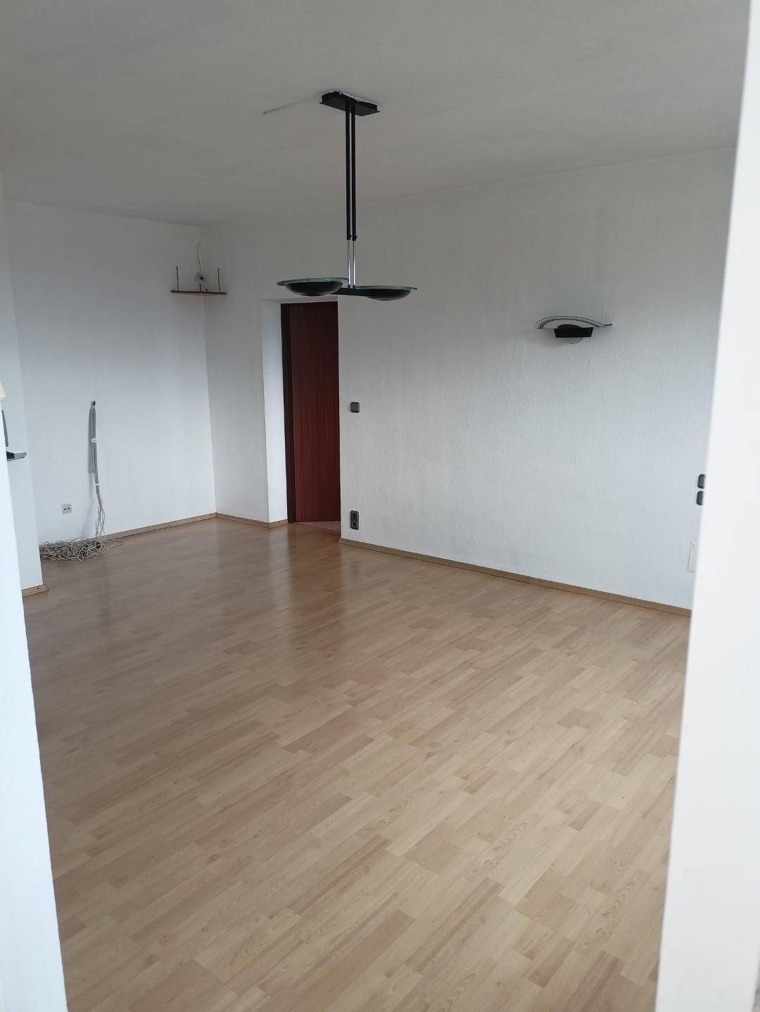 Geräumiges, unmöbliertes Wohnzimmer mit hellem Laminatboden und weiß gestrichenen Wänden.