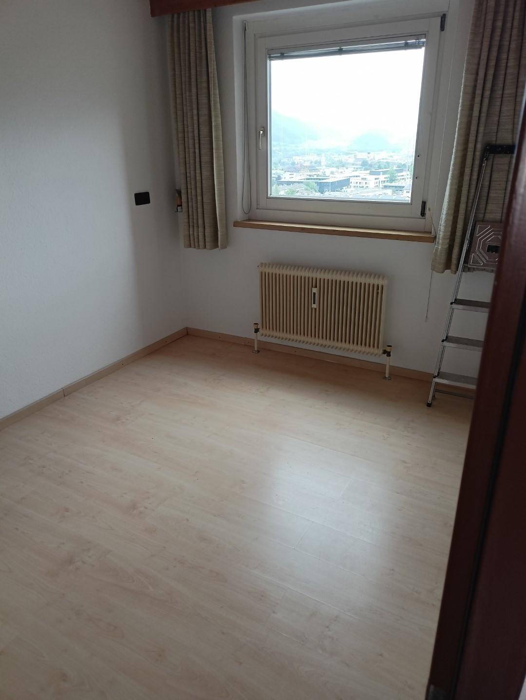Kleines, helles Schlafzimmer mit Laminatboden, Heizkörper und Fenster mit Stadtblick.