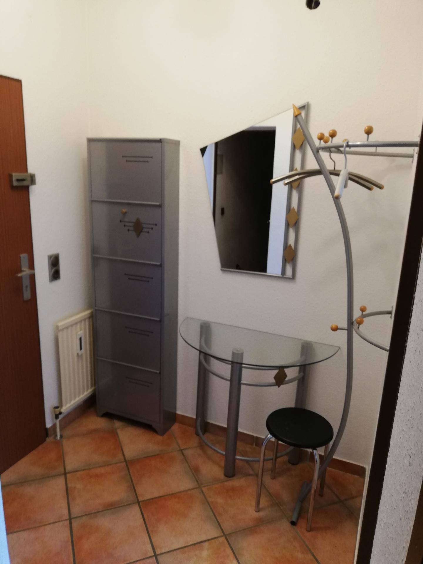 Flur mit Terrakotta-Fliesenboden, Spiegel, Konsole und Garderobe.