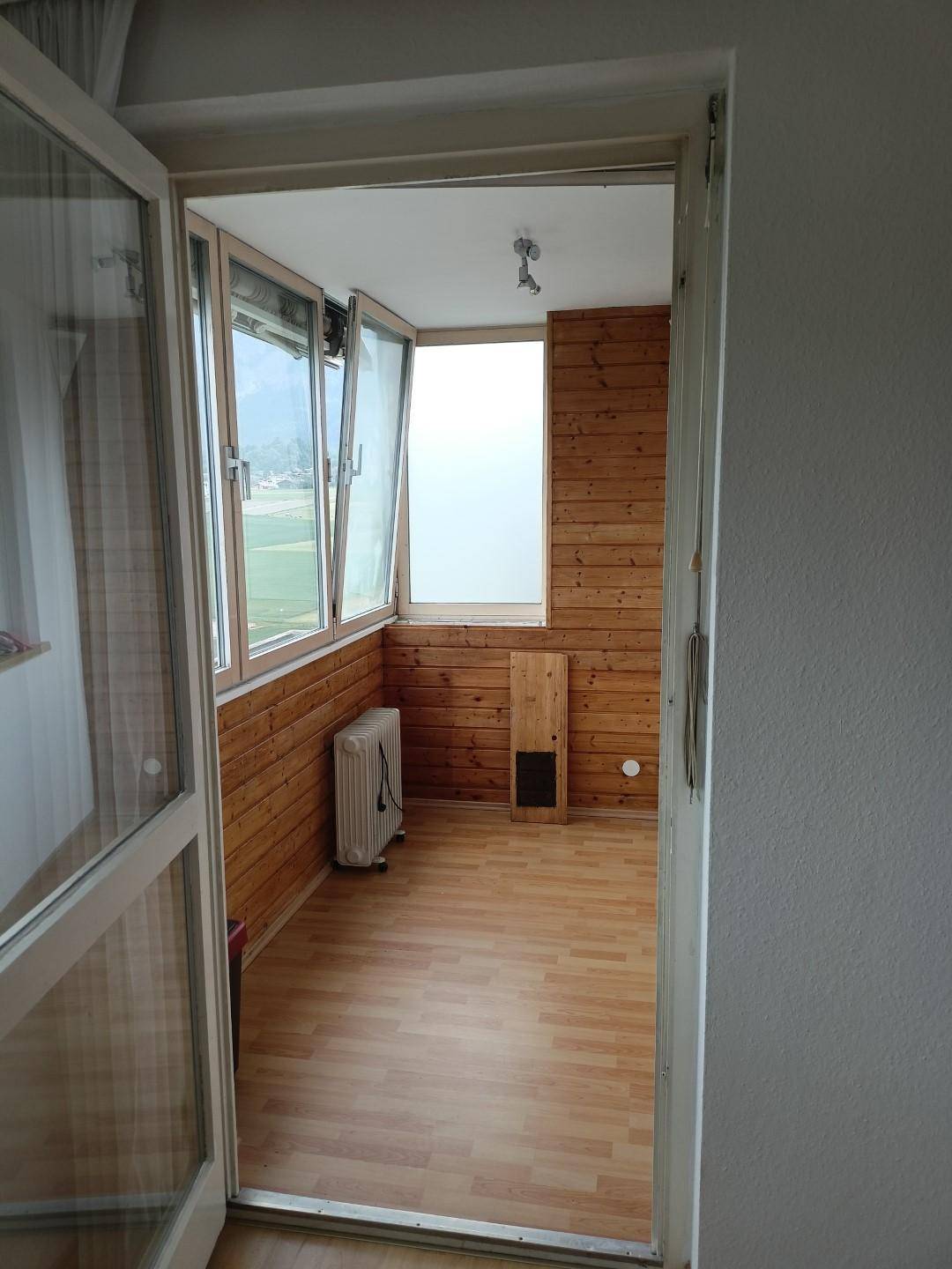 Helle, verglaste Loggia mit Holzverkleidung, Laminatboden und weitem Ausblick.
