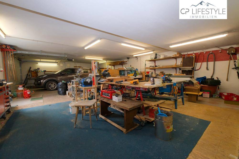 Geräumige Garage mit Werkstattbereich, Regalen und Platz für Fahrzeuge.
