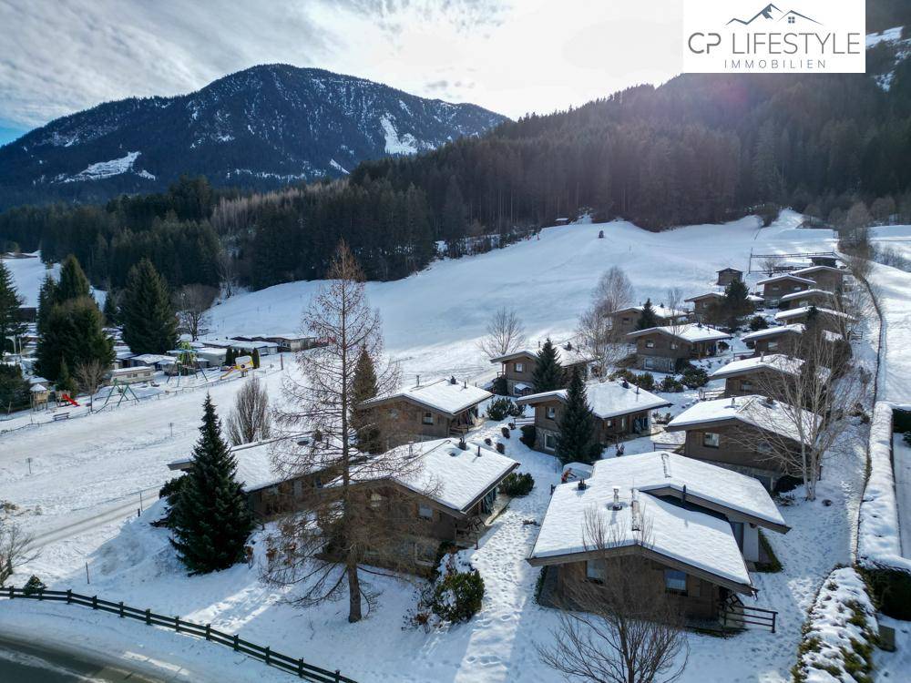 Panoramablick auf eine Ansammlung von verschneiten Chalets vor einer beeindruckenden Bergkulisse und weiten Schneefeldern.