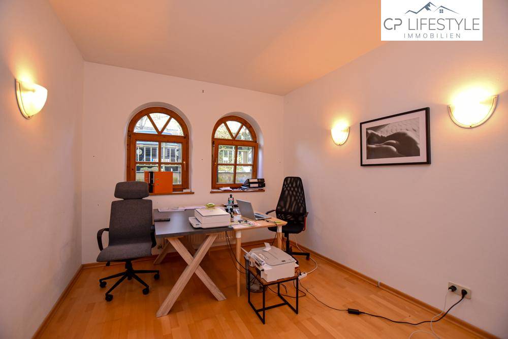 Arbeitszimmer mit zwei Rundbogenfenstern, Holzfußboden und indirekter Beleuchtung durch Wandlampen.