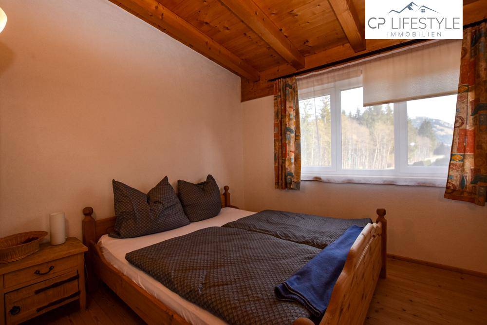 Gemütliches Schlafzimmer mit Holzbalkendecke, Doppelbett und Blick auf die umliegende Natur.