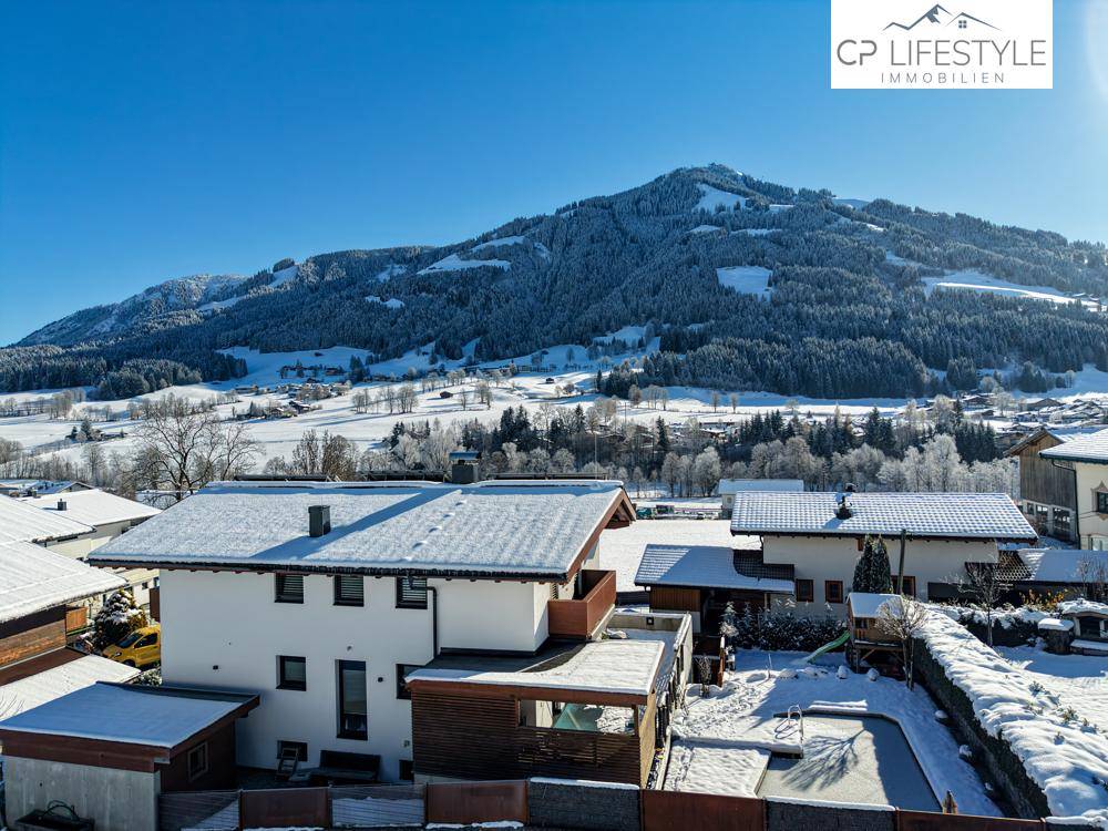 Verschneiter Gartenbereich mit Pool und umliegenden Häusern vor einer beeindruckenden Bergkulisse.