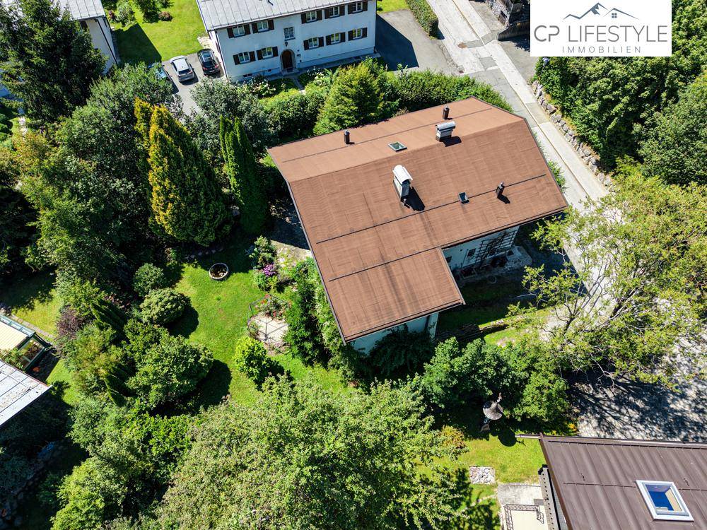 Vogelperspektive eines Einfamilienhauses mit großem Garten und umliegenden Bäumen.