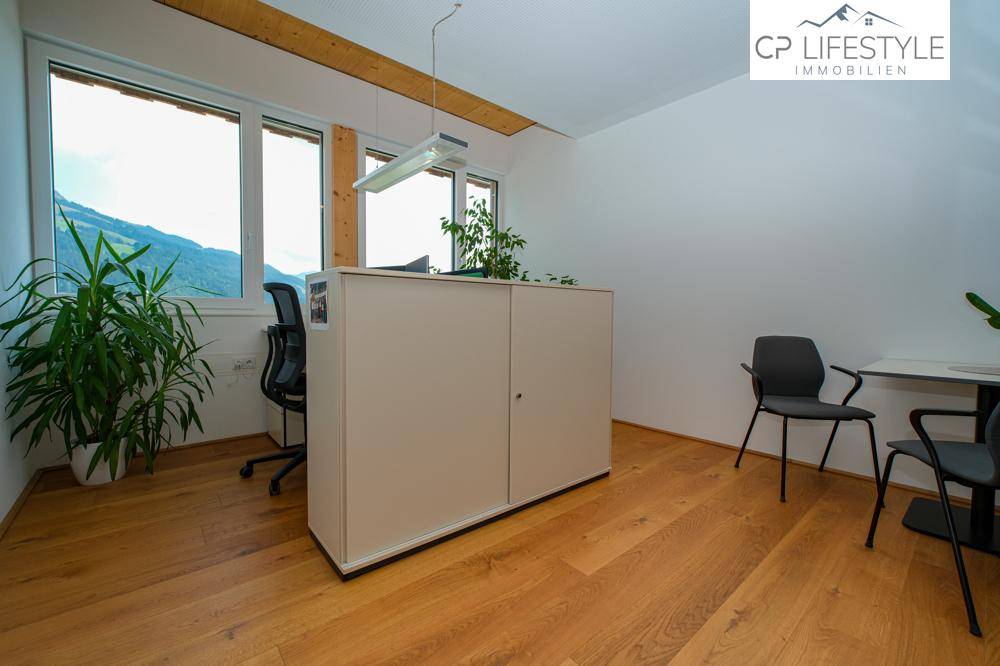 Geräumiges Büro mit Holzboden, Pflanzen und großen Fenstern, die viel Tageslicht hereinlassen.