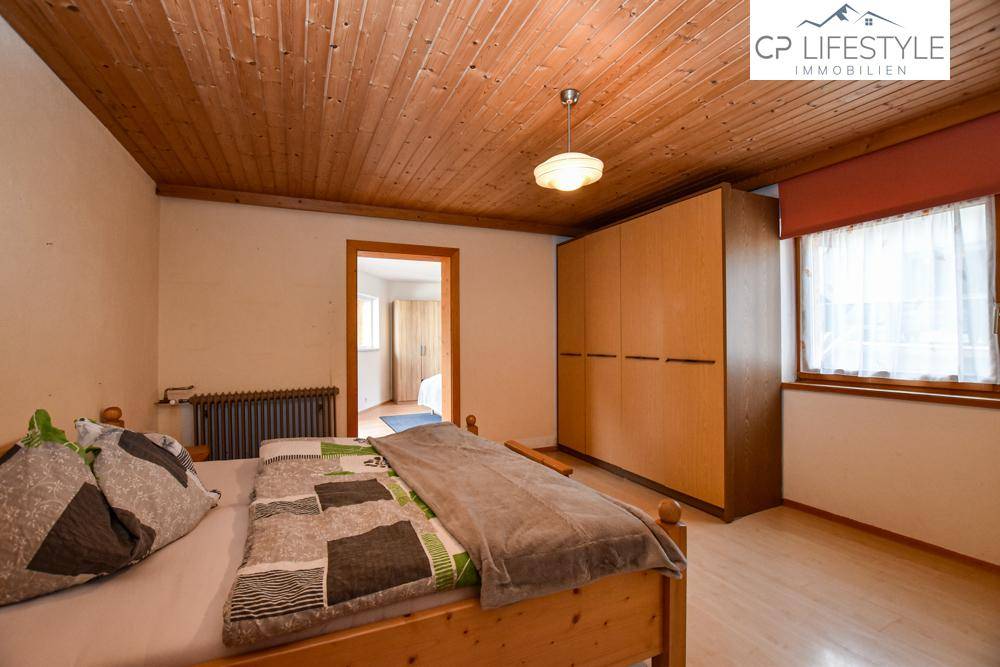Helles Schlafzimmer mit Holzbalkendecke, Holzschrank und Blick ins Grüne.