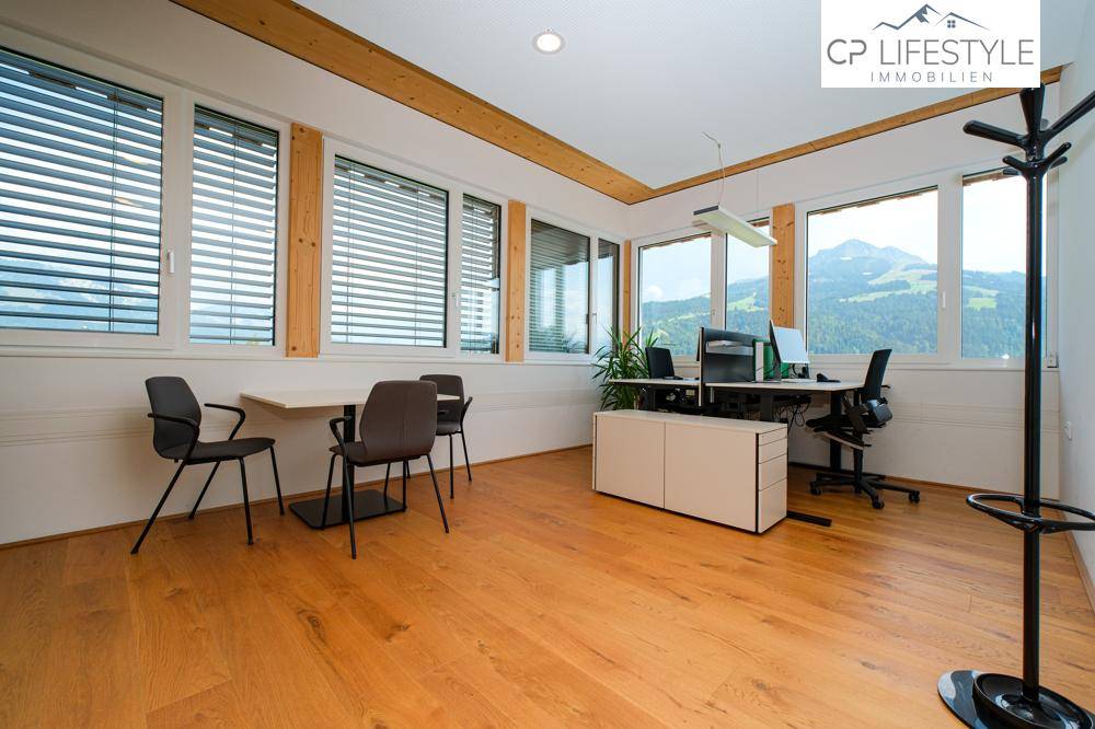 Helles Büro mit Holzboden, großen Fenstern und Blick auf die umliegende Berglandschaft.