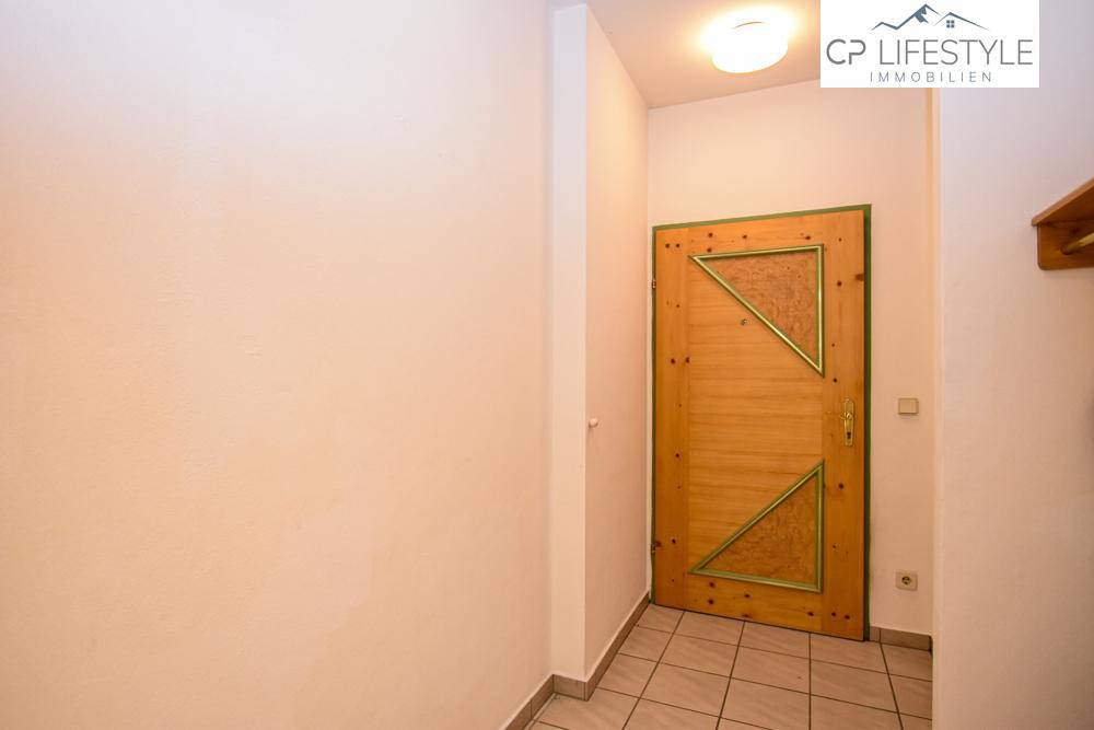 Eingangsbereich mit gefliestem Boden und einer traditionellen Holztür mit dekorativen Elementen.