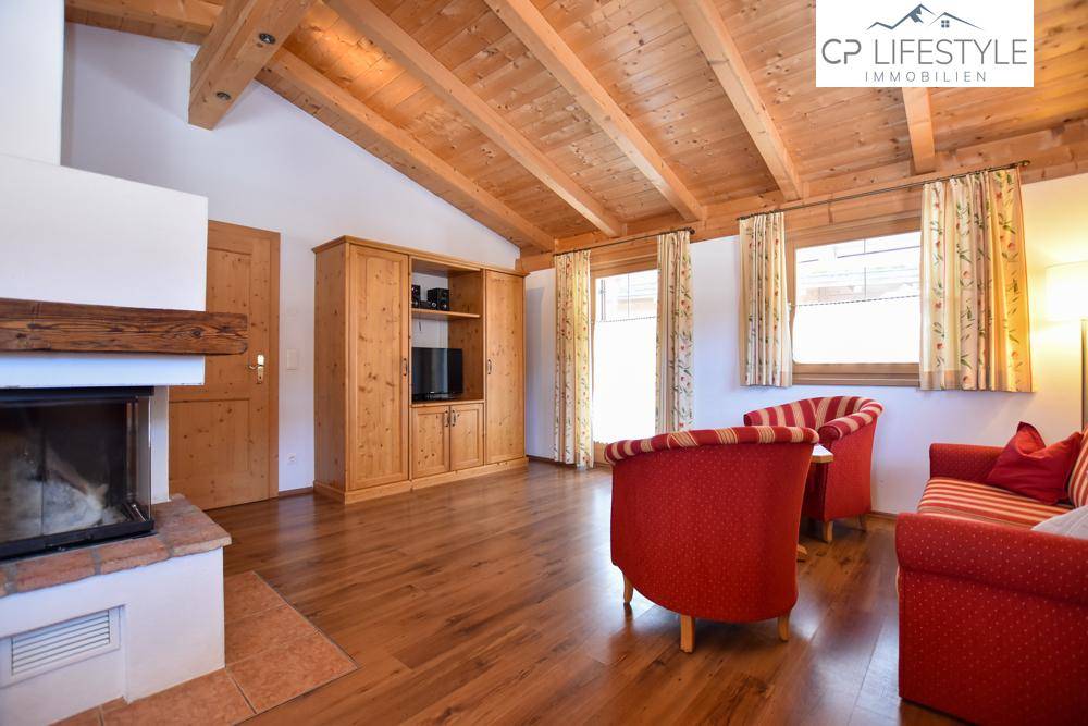 Rustikales Wohnzimmer mit Holzbalkendecke, Kamin und bequemen roten Sitzmöbeln, ideal für entspannte Abende.