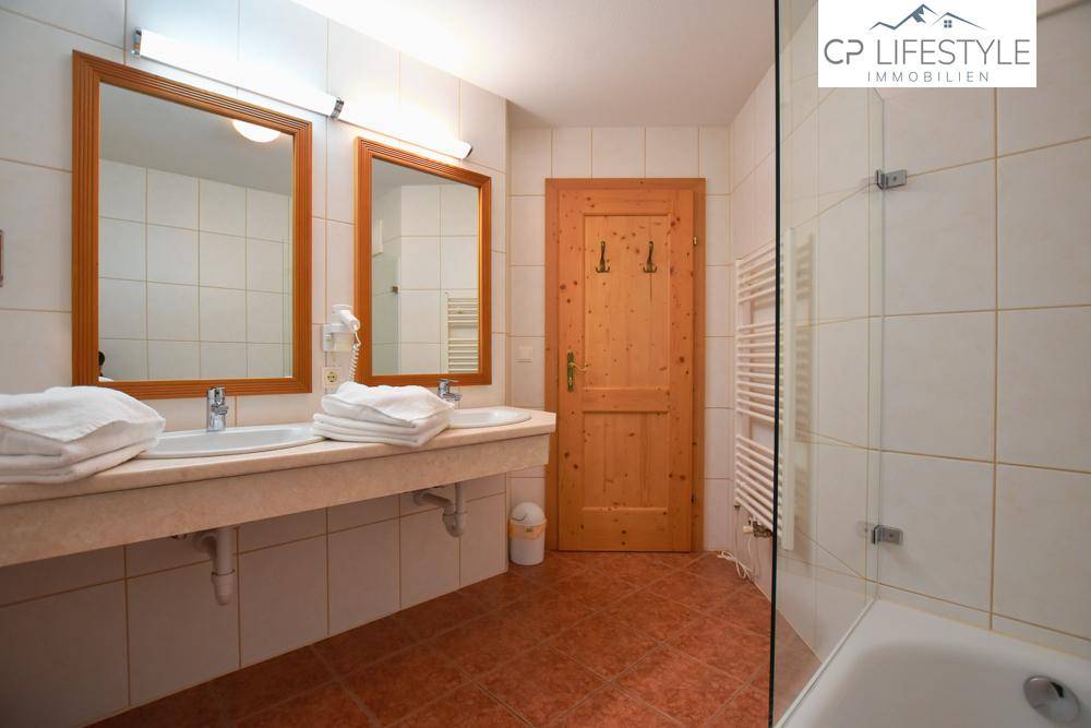 Funktionelles Badezimmer mit Doppelwaschbecken, Dusche und beheiztem Handtuchhalter, in hellem Design gehalten.