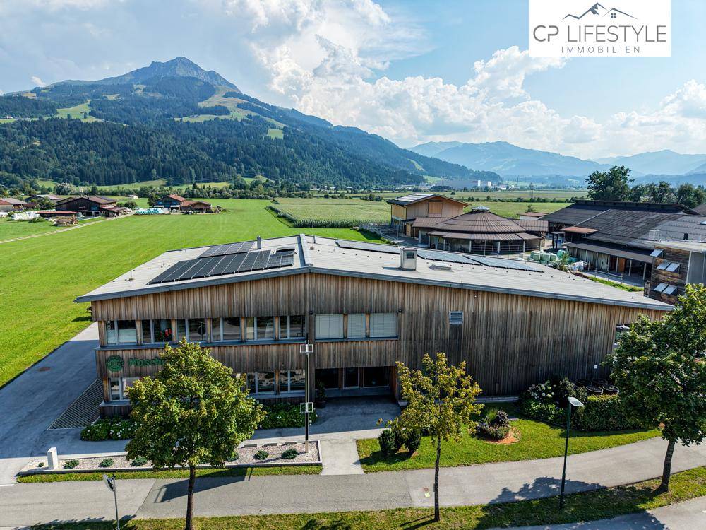 Luftaufnahme des modernen Geschäftsgebäudes mit Holzfassade, Solaranlage und weitem Blick auf die Berglandschaft.