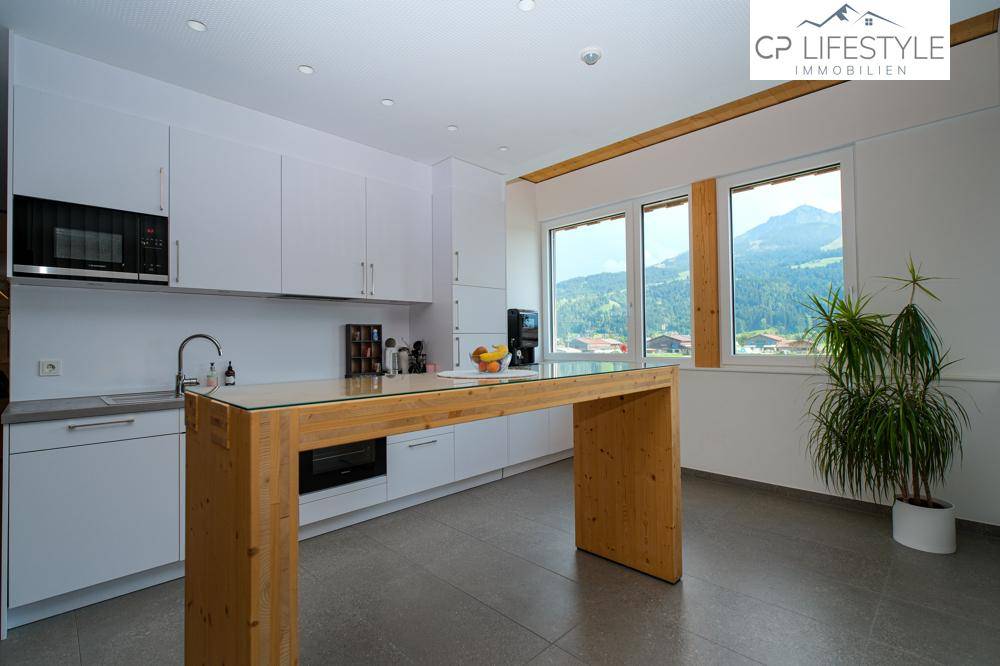Moderne Einbauküche mit weißen Schränken, Holztresen und Blick auf die Berglandschaft.
