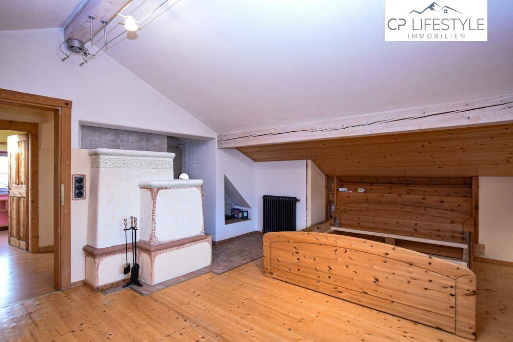 Dachgeschoss-Schlafzimmer mit Holzboden, Kachelofen und rustikalem Charme.