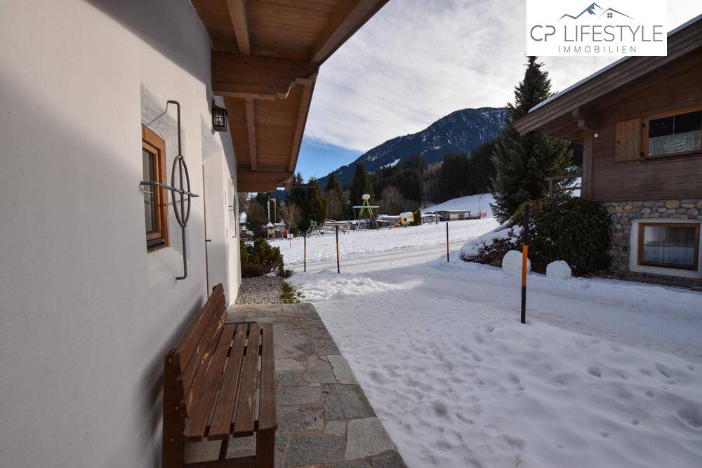 Eingangsbereich eines Chalets mit einer Holzbank und einem verschneiten Weg, der zur Unterkunft führt.