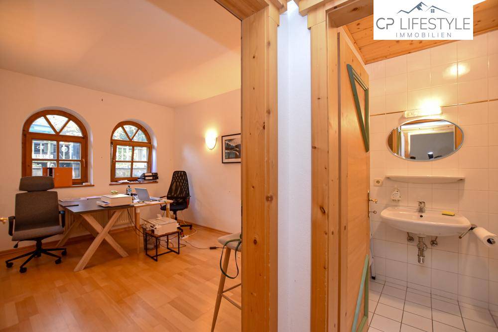 Büro mit Rundbogenfenstern und offenem Zugang zu einem angrenzenden Badezimmer mit Waschbecken.